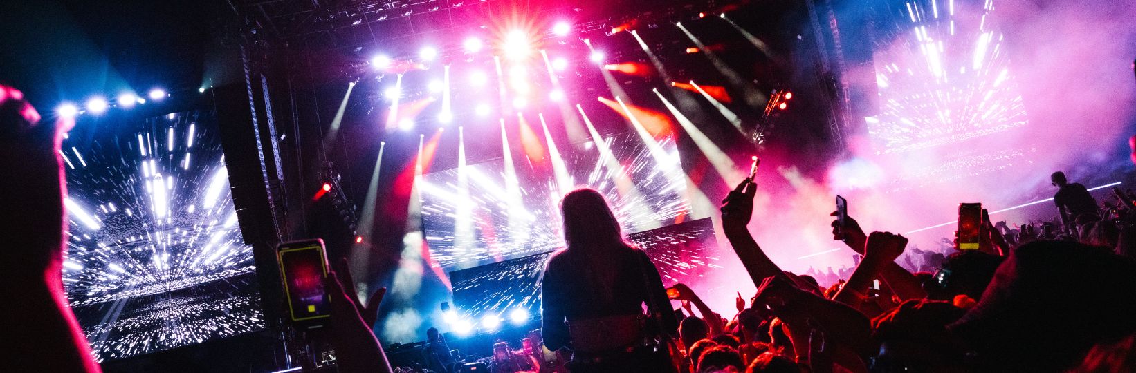 Image of stage with people on shoulders in the crowd, bright pink, red and white lights