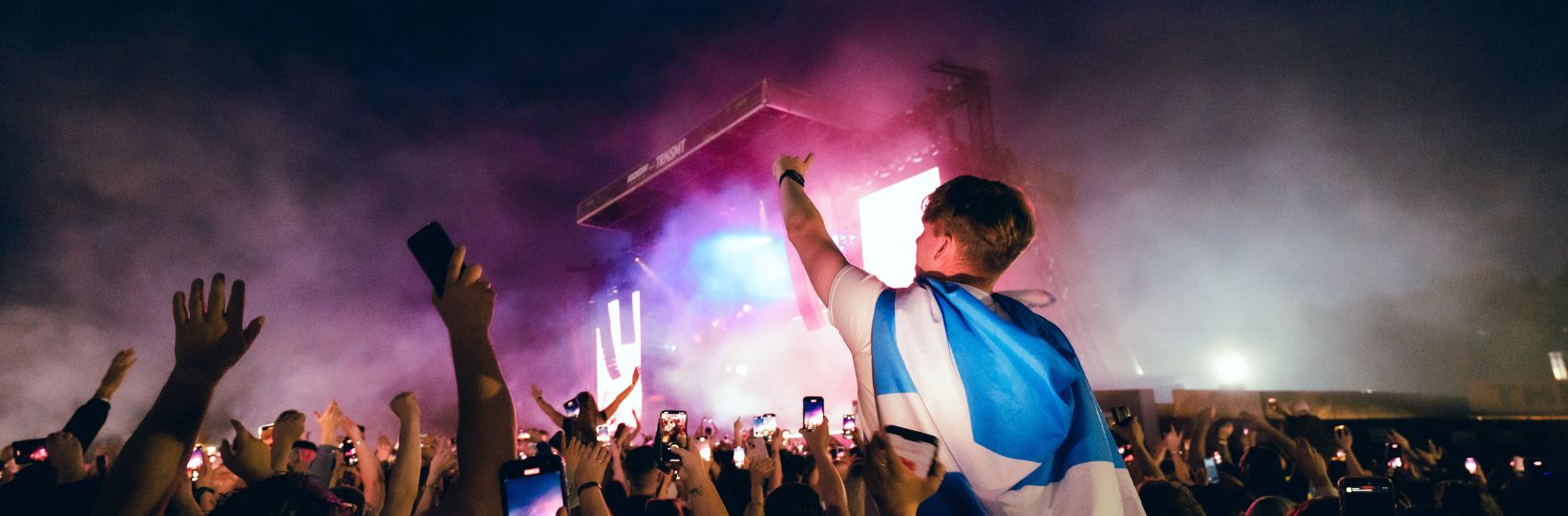 View of Main Stage, audience members have their hands in the air and one member is on shoulders with scotland flag round their neck.