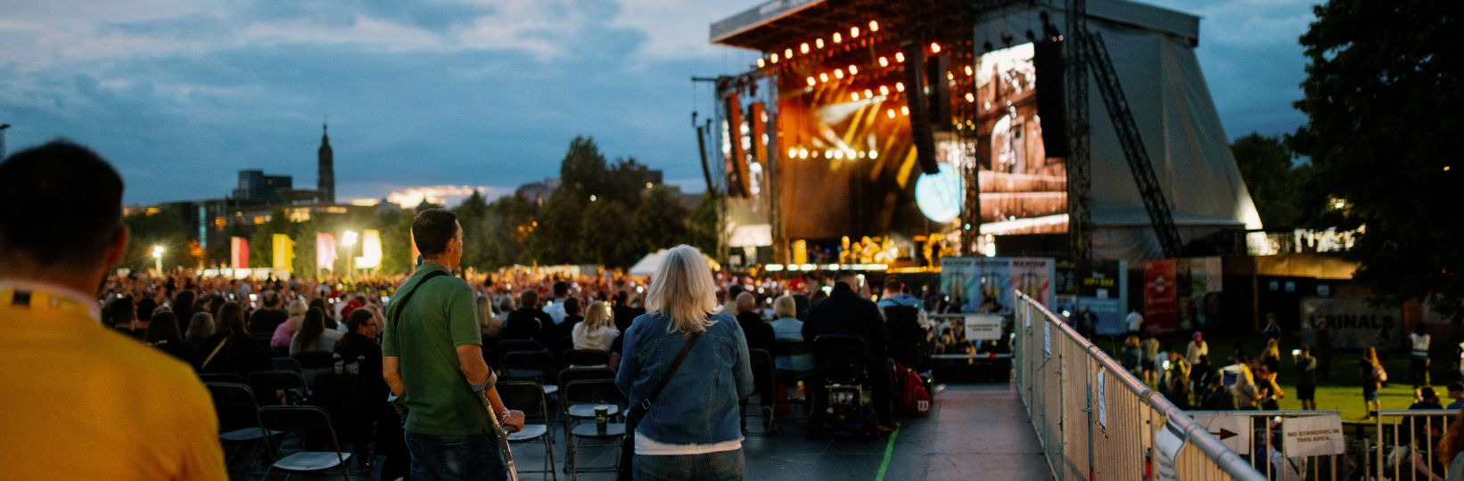 The accessibility platform at the festival with people both sitting and standing watching the band perform on the main stage